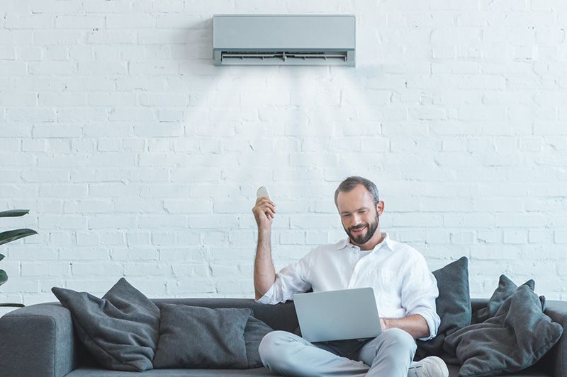 man sitting on couch using laptop under ductless vent.