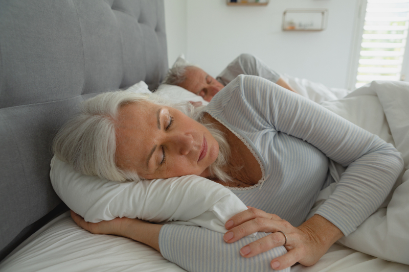 3 Health Benefits of Using Your AC While Sleeping. Photo of an elderly couple sleeping soundly in their bed.