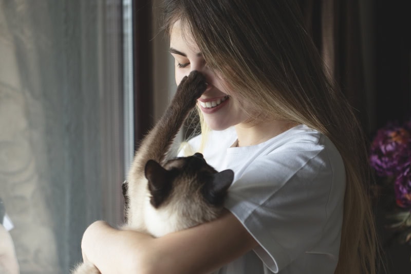Transitioning Your Heat Pump. Young woman hugging her cat in front of the window