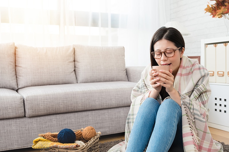 Young woman warming up with a blanket & a cup of hot cocoa, Why Is My Heat Pump Blowing Cold Air? | HVAC Repair | Westford, MA