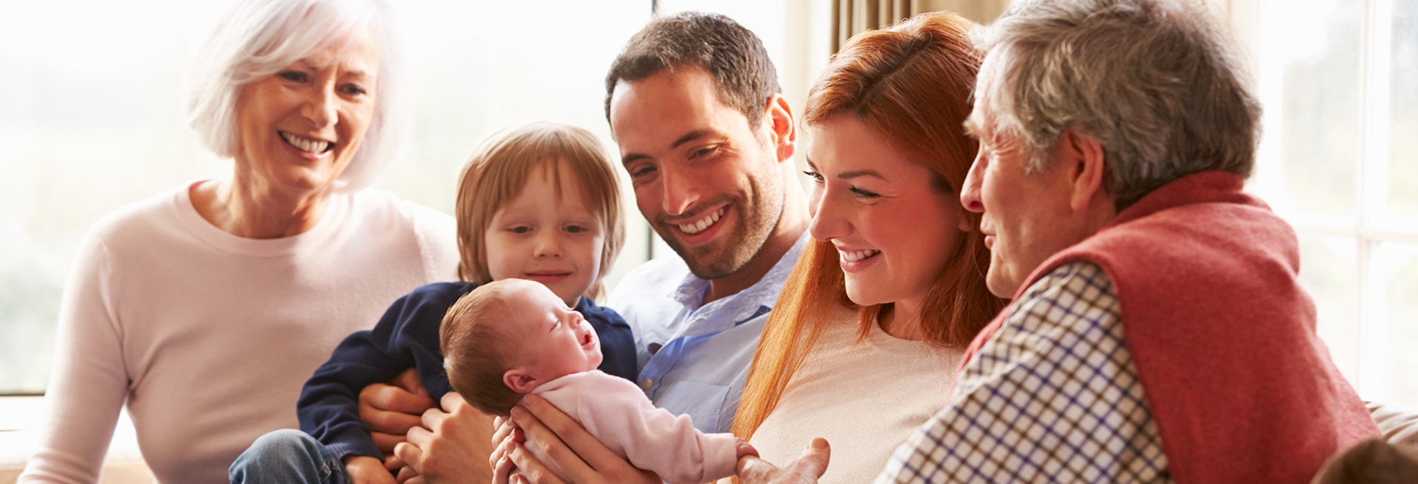 Multi-generation family sitting on sofa with newborn baby.