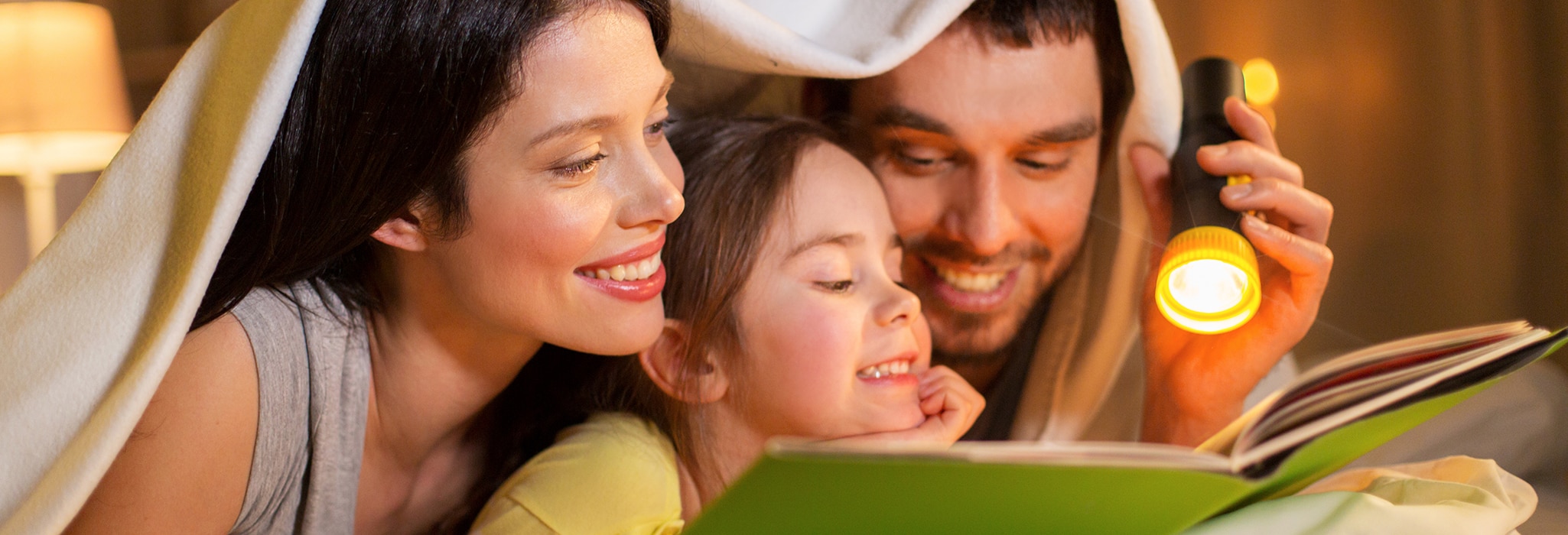 Happy family reading book in bed at night at home.
