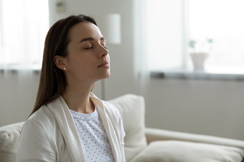 woman sitting on her couch while taking a deep breath.