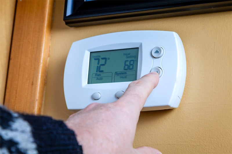 A person lowers temperature on a home thermostat, Why a Higher Setting on the Thermostat in Summer Is Better | Basnett