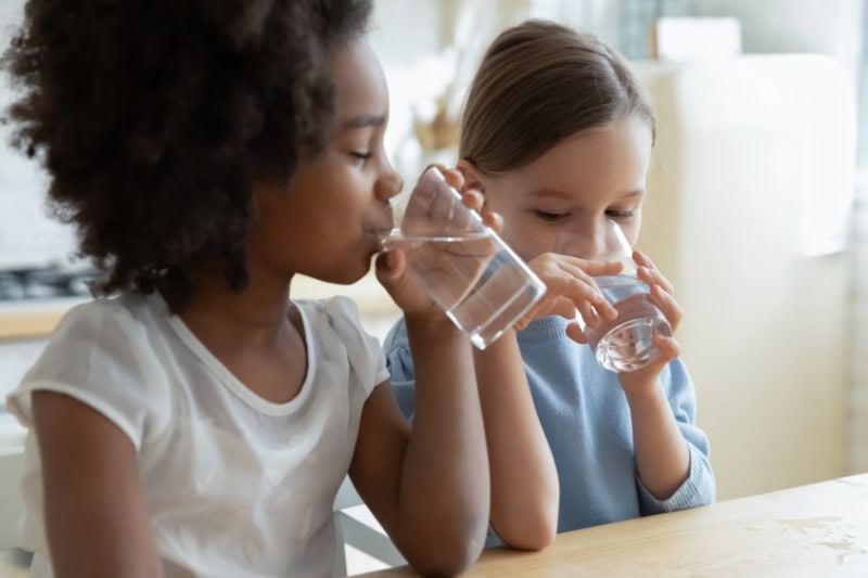 2 young girl drinking water out of a glass.