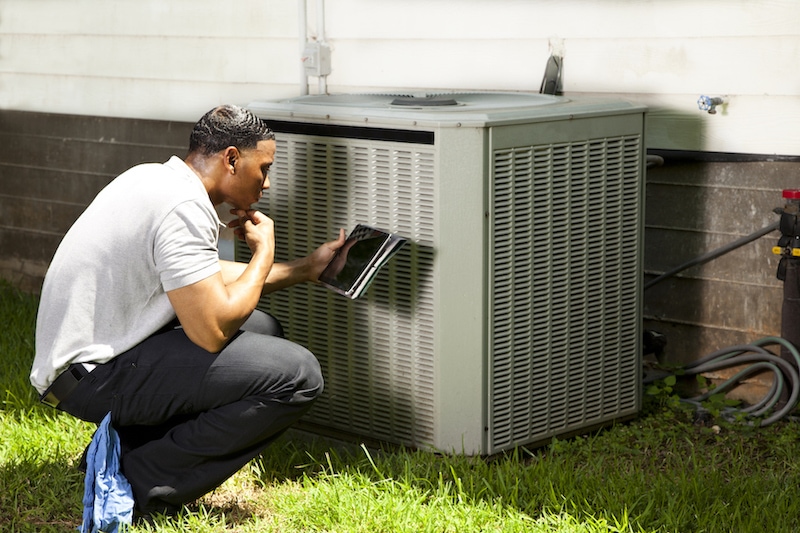 Home inspector, repairman, adjuster examines air conditioner units at a customer home. He is using his digital tablet to record results. AC Maintenance