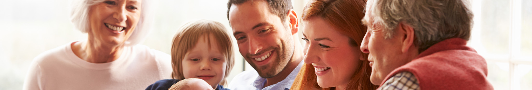 Multi Generation Family Sitting On Sofa With Newborn Baby Smiling