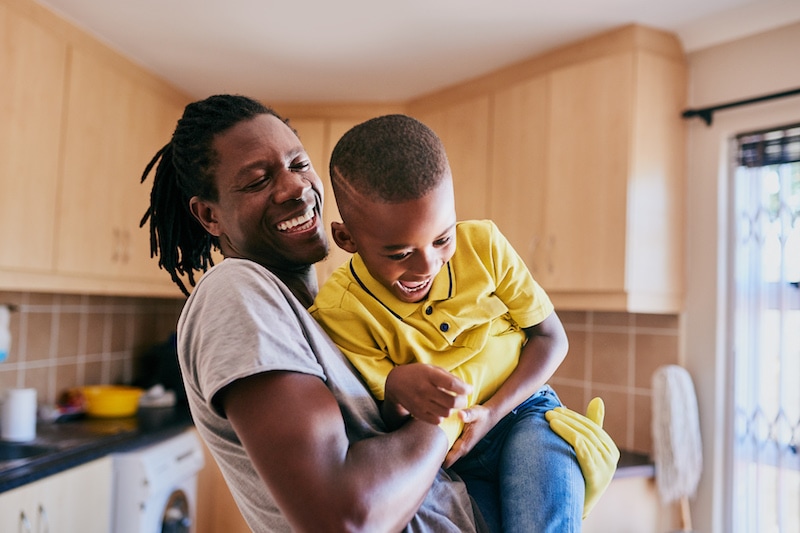 young single father playing with his son while cleaning in their kitchen at home