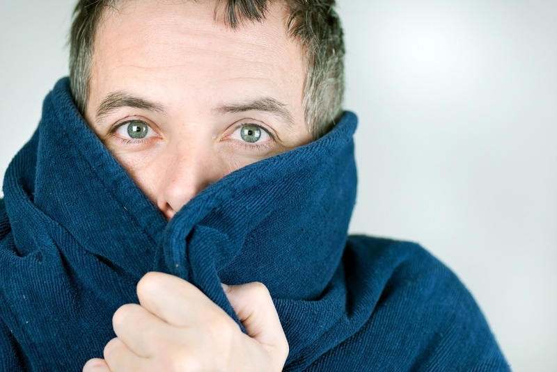 Middle aged white man with green eyes wrapping a blue blanket around his shoulders and face, Uneven Heating