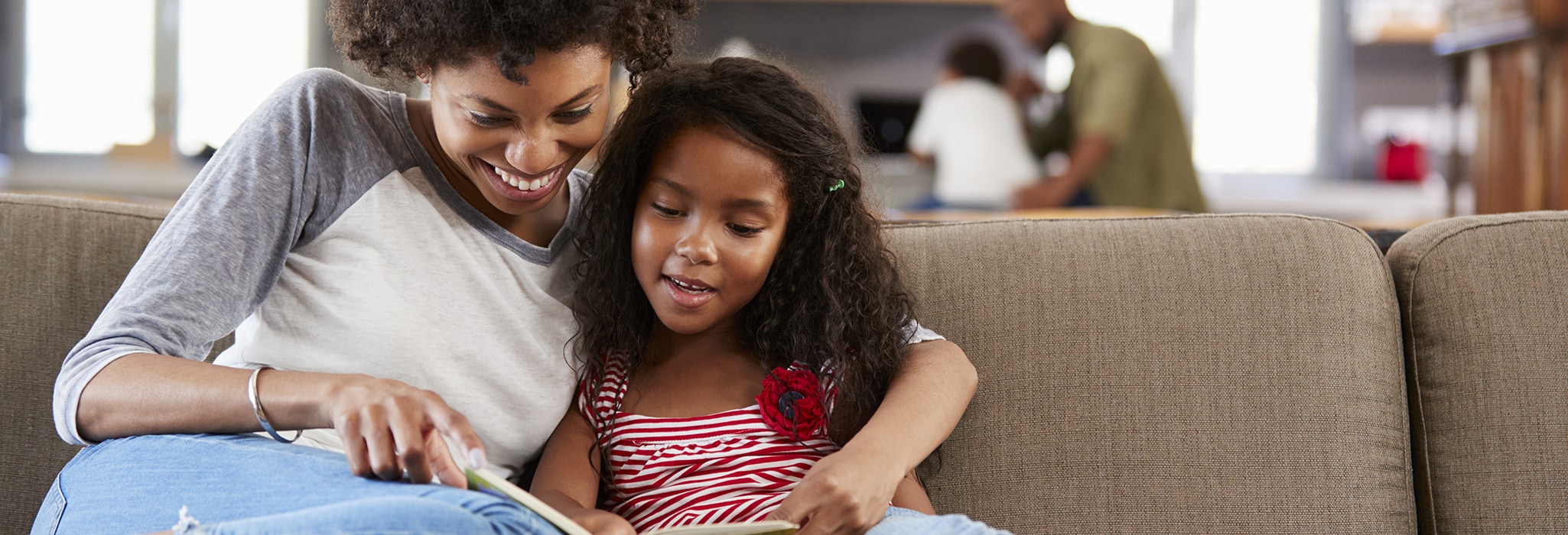 Mother and daughter reading book on the couch.