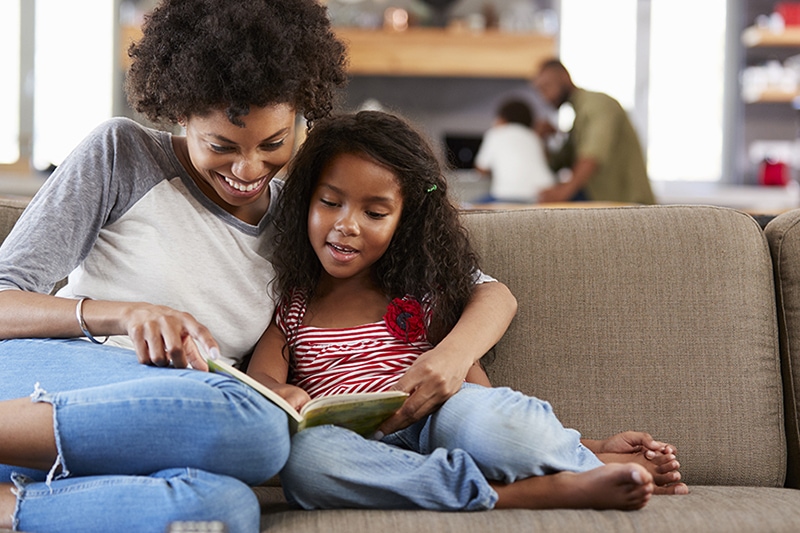 Mother And Daughter Sit On Sofa In Lounge Reading Book Together. Understanding biofuel.