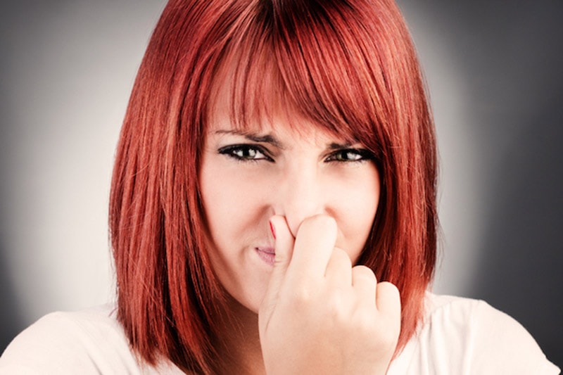 A young girl with short brown hair wearing a gray top pinching her nose with her right hand