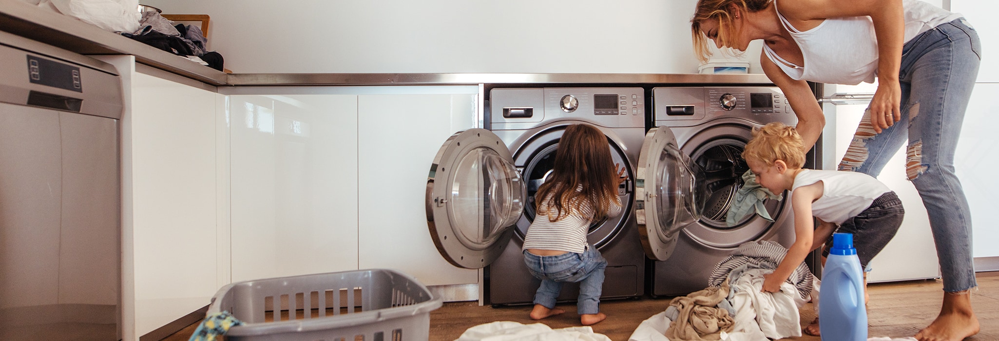 Mother and children putting laundry into washing machine at home.